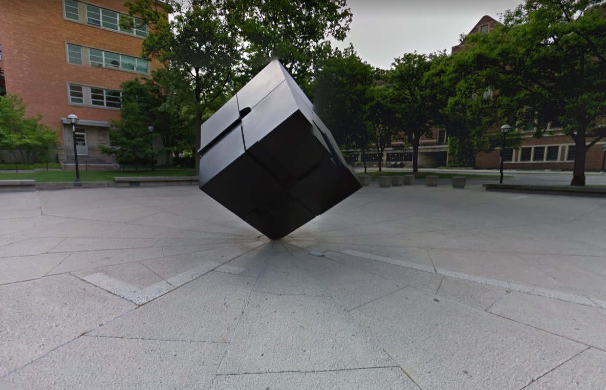 Image of a statue of a black cube, balanced on one of its corners in a university plaza